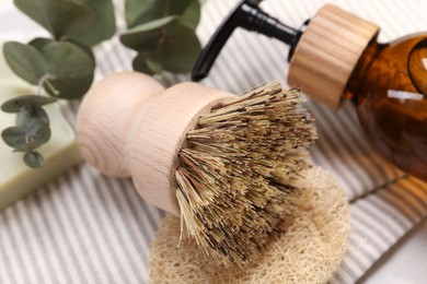 Photo of Cleaning brush, sponge, dispenser and eucalyptus leaves on table, closeup