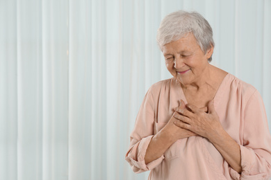 Photo of Grateful senior woman with hands on chest against light background. Space for text