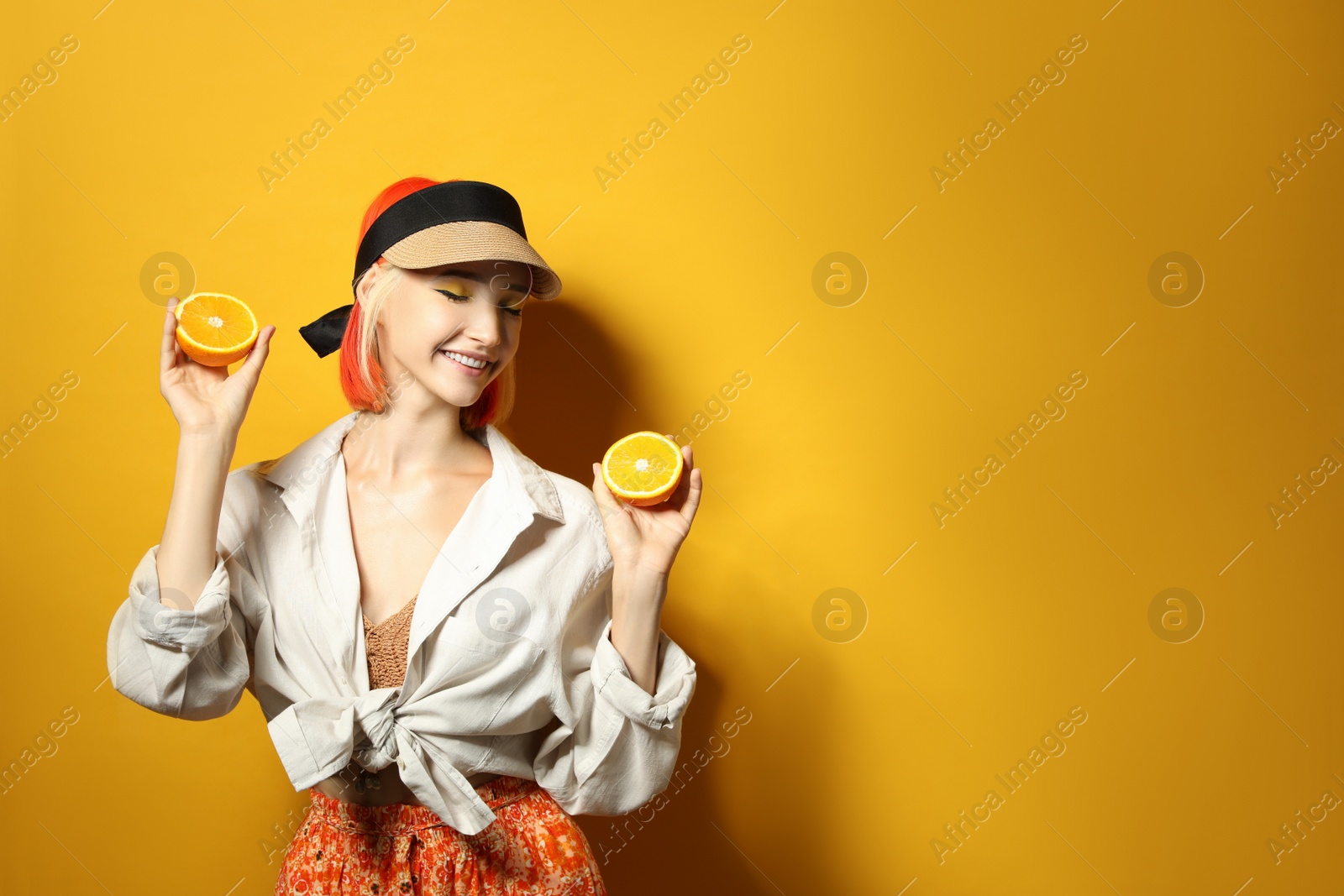 Photo of Beautiful young woman with bright dyed hair holding orange halves on color background