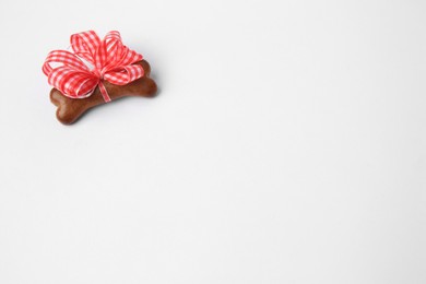 Photo of Bone shaped dog cookie with red bow on white background, top view. Space for text
