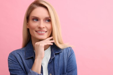 Portrait of smiling middle aged woman with blonde hair on pink background. Space for text