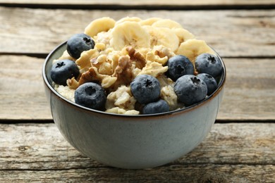 Photo of Tasty oatmeal with banana, blueberries and walnuts served in bowl on wooden table