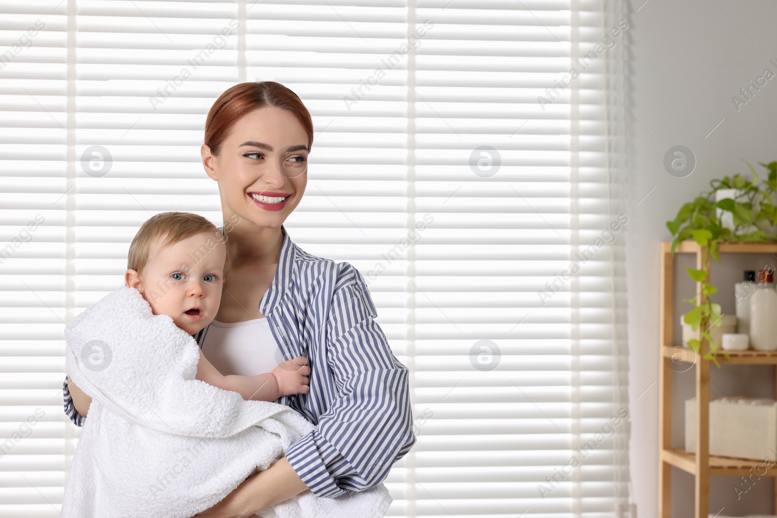 Photo of Mother holding cute little baby wrapped with towel after bath indoors. Space for text