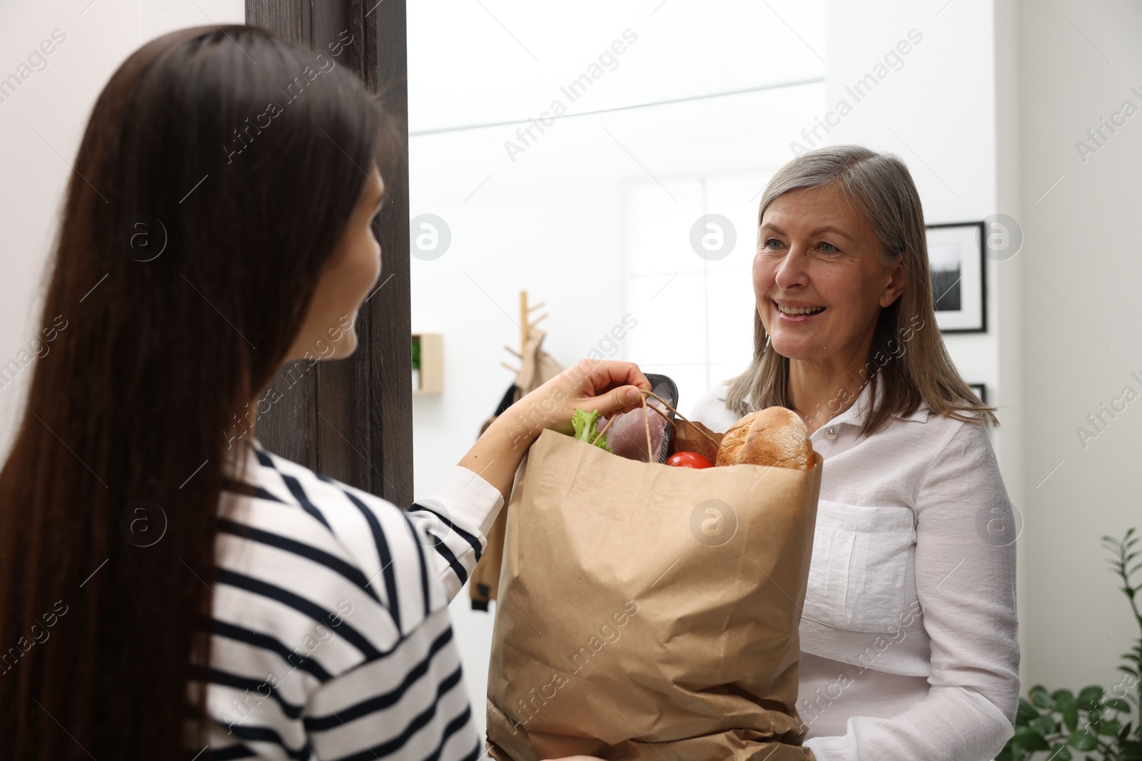 Photo of Courier giving paper bag with food products to senior woman indoors