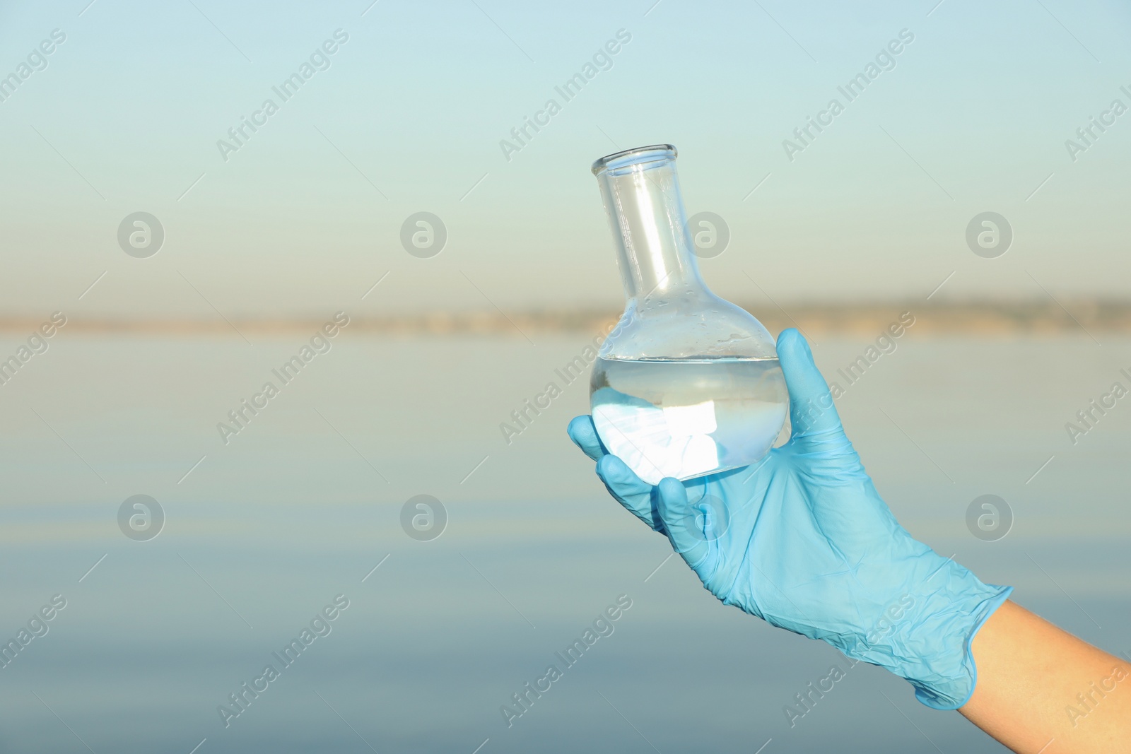 Photo of Scientist with florence flask taking sample from river for analysis, closeup