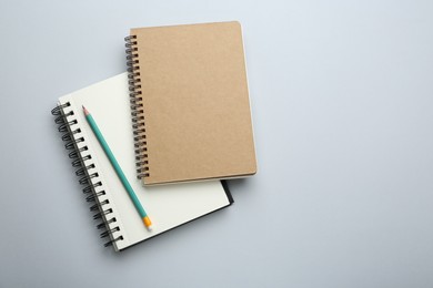 Photo of Notebooks and pencil on light grey background, top view. Space for text