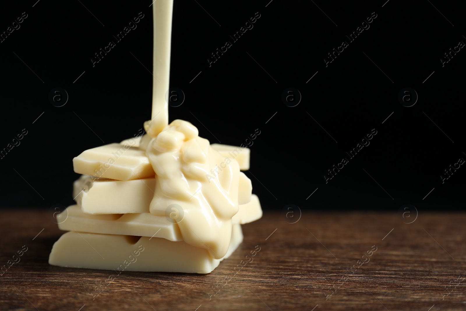 Photo of Pouring tasty white chocolate paste onto pieces on wooden table, closeup. Space for text