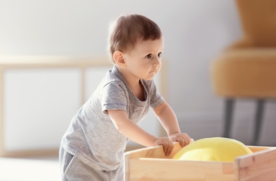 Photo of Cute baby holding on to wooden cart indoors. Learning to walk