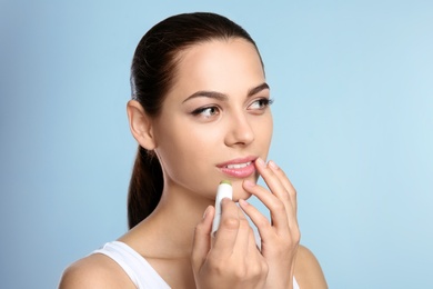 Photo of Young woman applying balm on her lips against color background