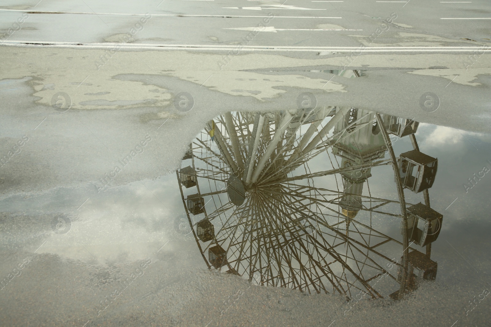 Photo of Reflection of Ferris wheel in puddle on asphalt outdoors