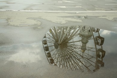 Photo of Reflection of Ferris wheel in puddle on asphalt outdoors