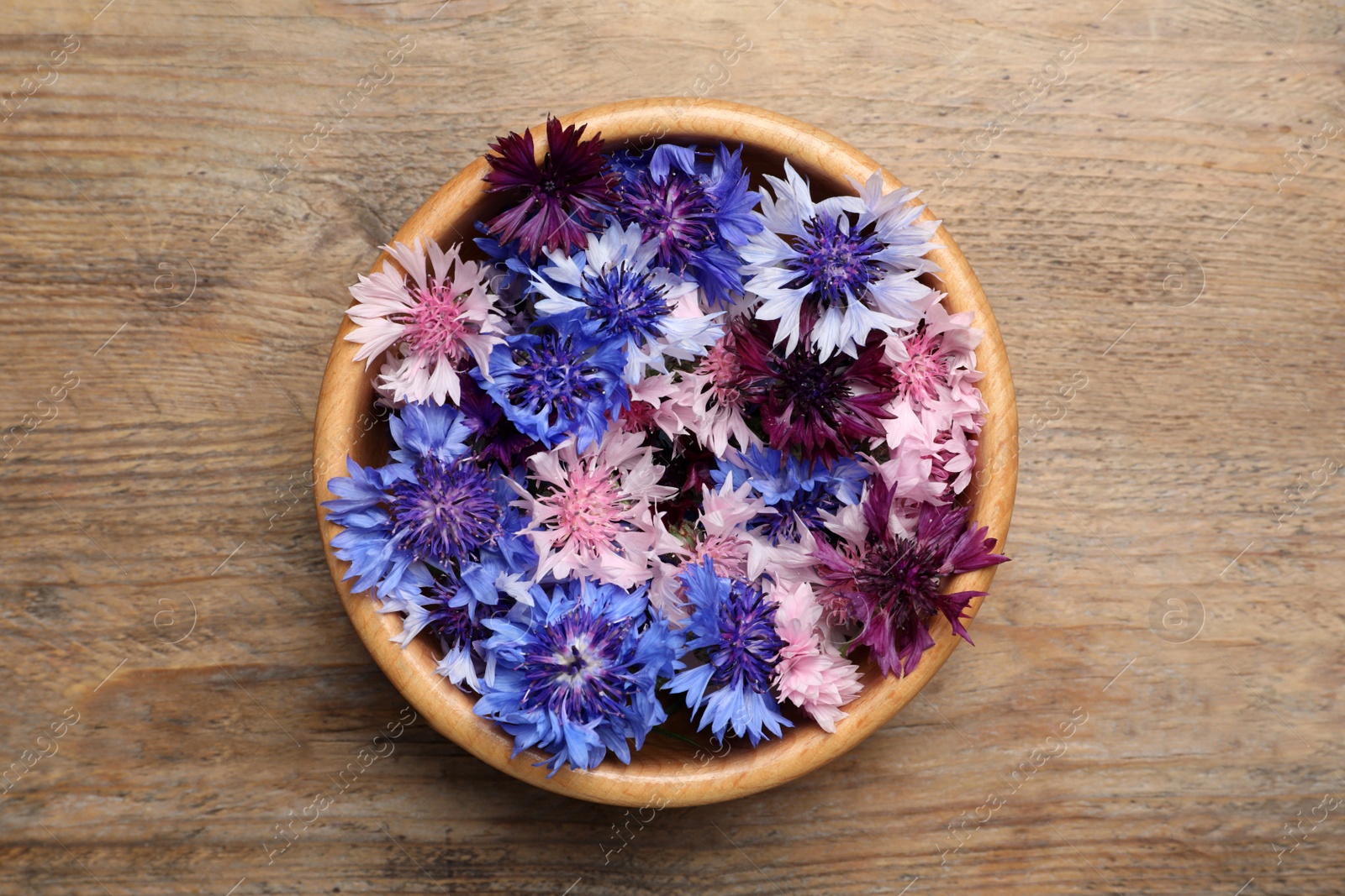 Photo of Beautiful colorful cornflowers in bowl on wooden table, top view