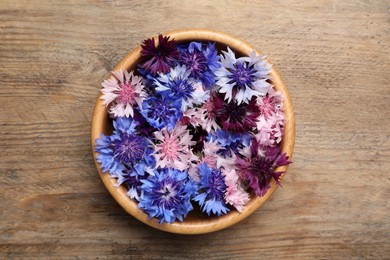 Beautiful colorful cornflowers in bowl on wooden table, top view