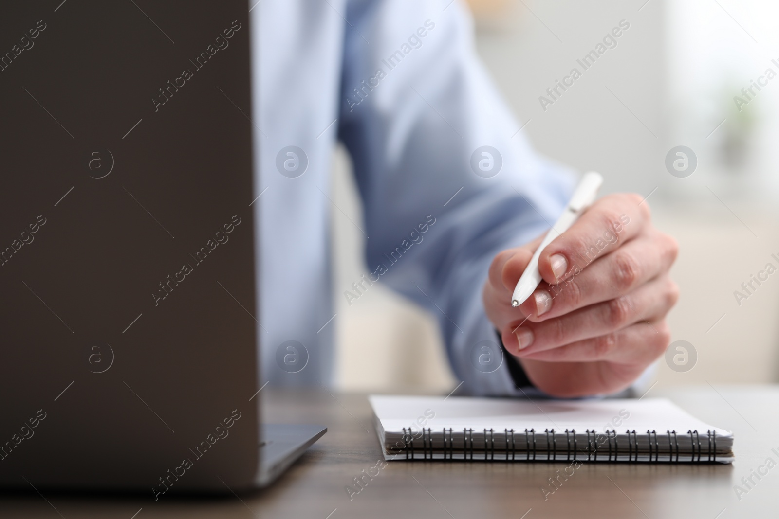 Photo of E-learning. Man taking notes during online lesson at table indoors, closeup