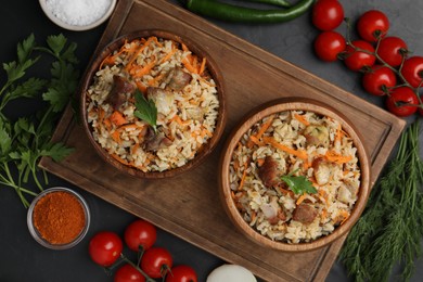 Delicious pilaf in bowls and products on black table, flat lay