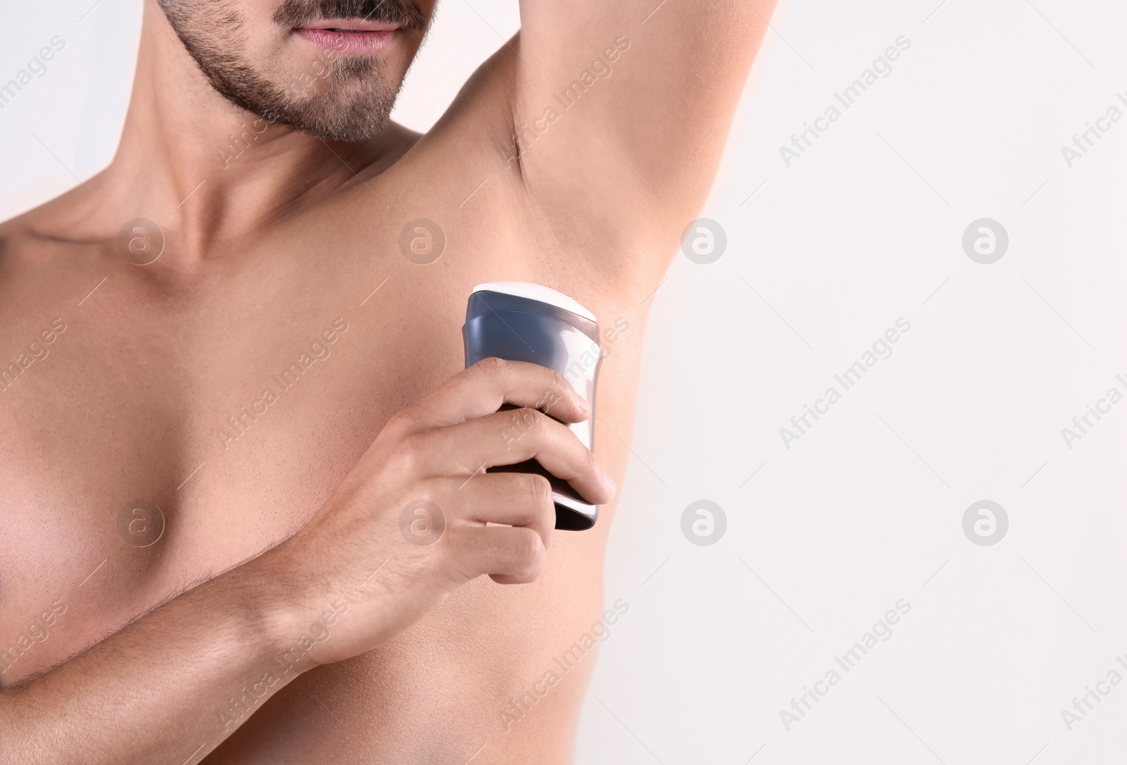 Photo of Young man using deodorant on white background, closeup. Space for text