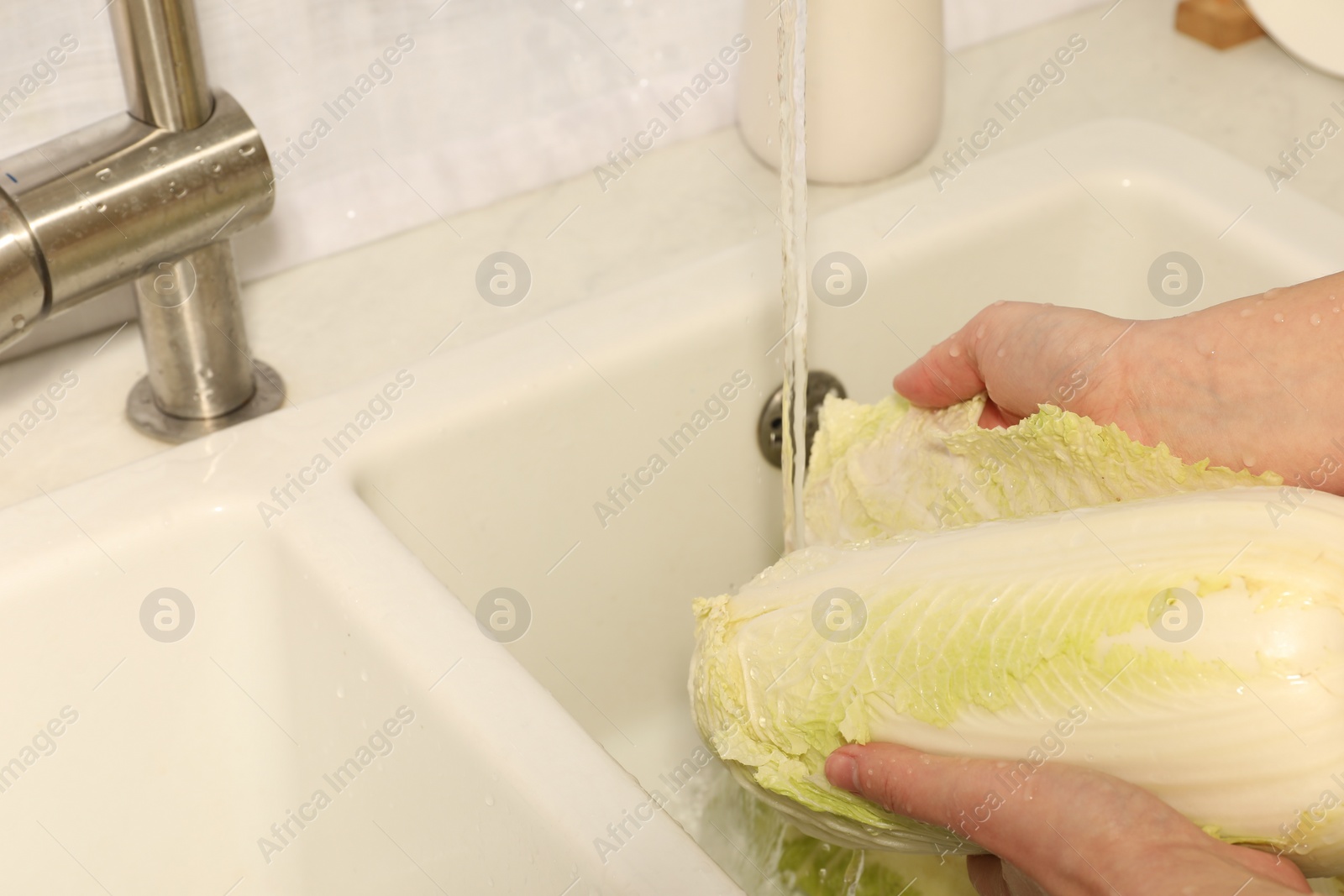 Photo of Woman washing fresh chinese cabbage under tap water in kitchen sink, closeup