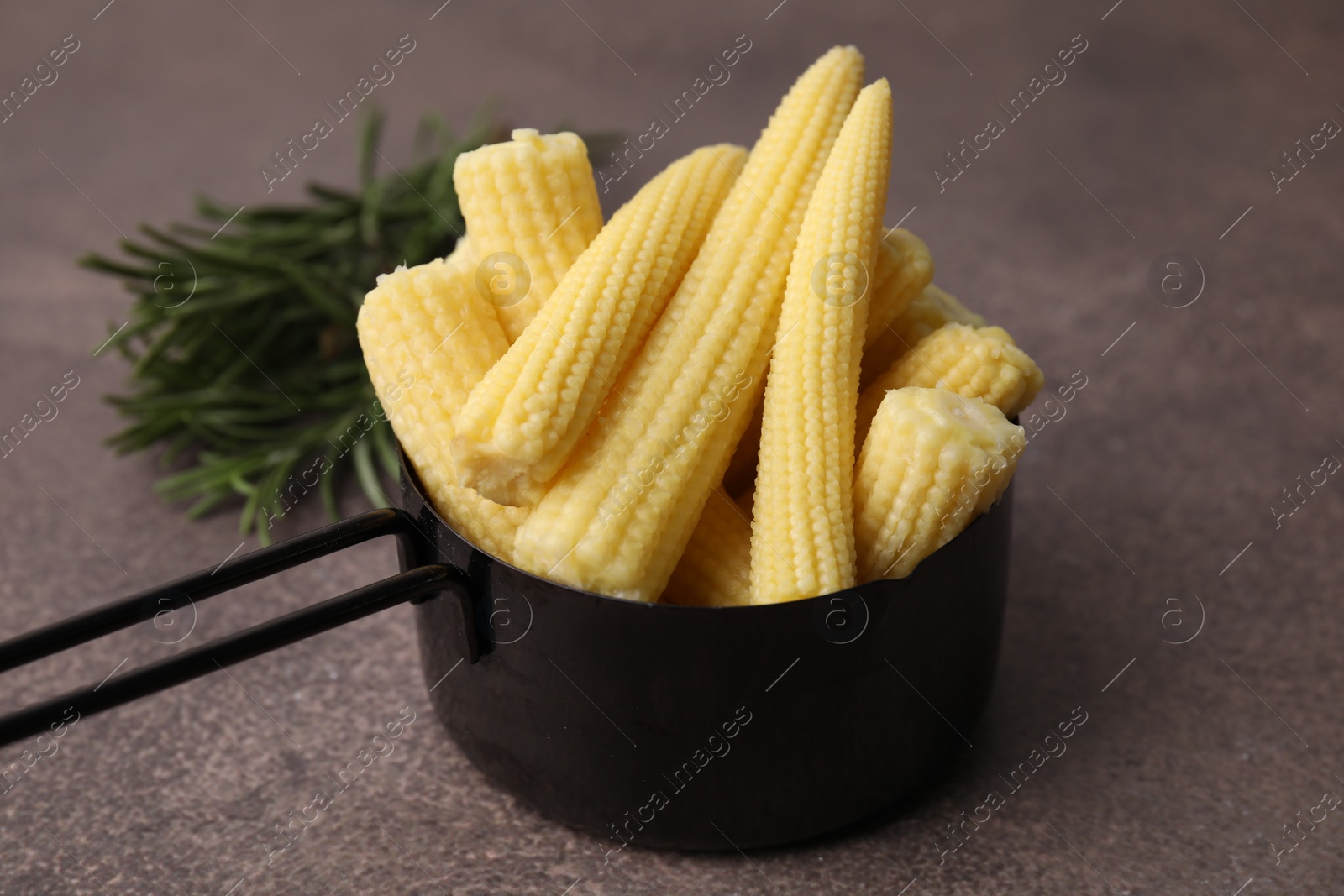 Photo of Tasty fresh yellow baby corns in dish on brown table, closeup