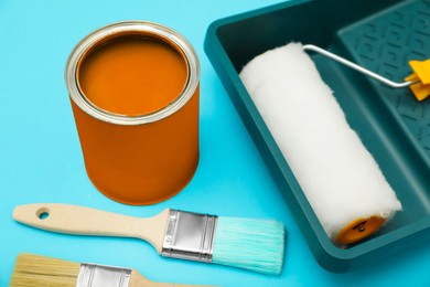 Photo of Can of orange paint, brushes, roller and container on turquoise background, closeup