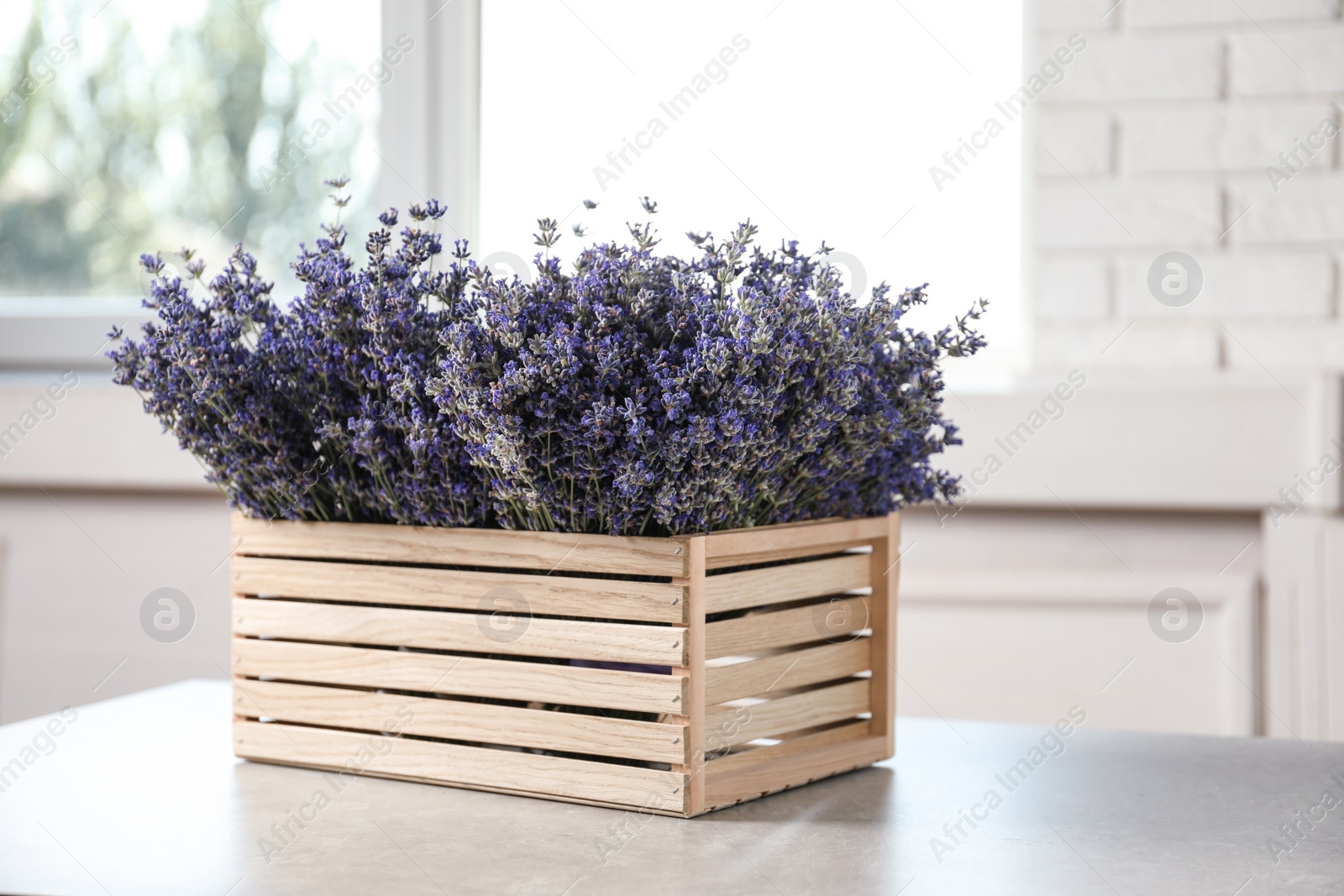 Photo of Fresh lavender flowers in wooden crate on stone table indoors, space for text