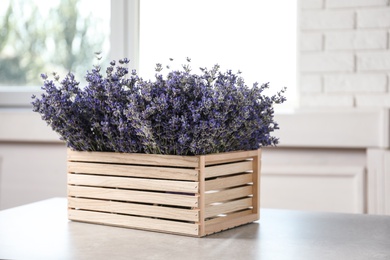 Fresh lavender flowers in wooden crate on stone table indoors, space for text