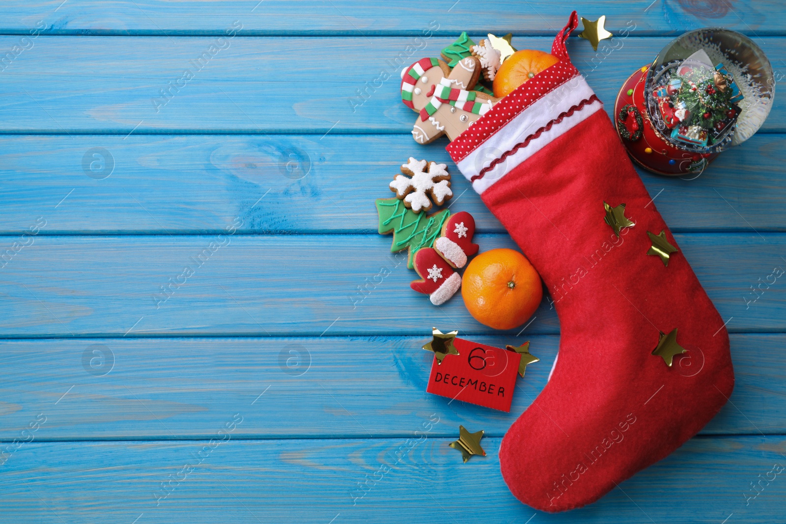 Photo of December, 6 - Saint Nicholas Day. Stocking with sweets, paper tag, festive decor and space for text on blue wooden table, flat lay