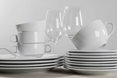 Photo of Set of clean dishware and glasses on white wooden table against light background