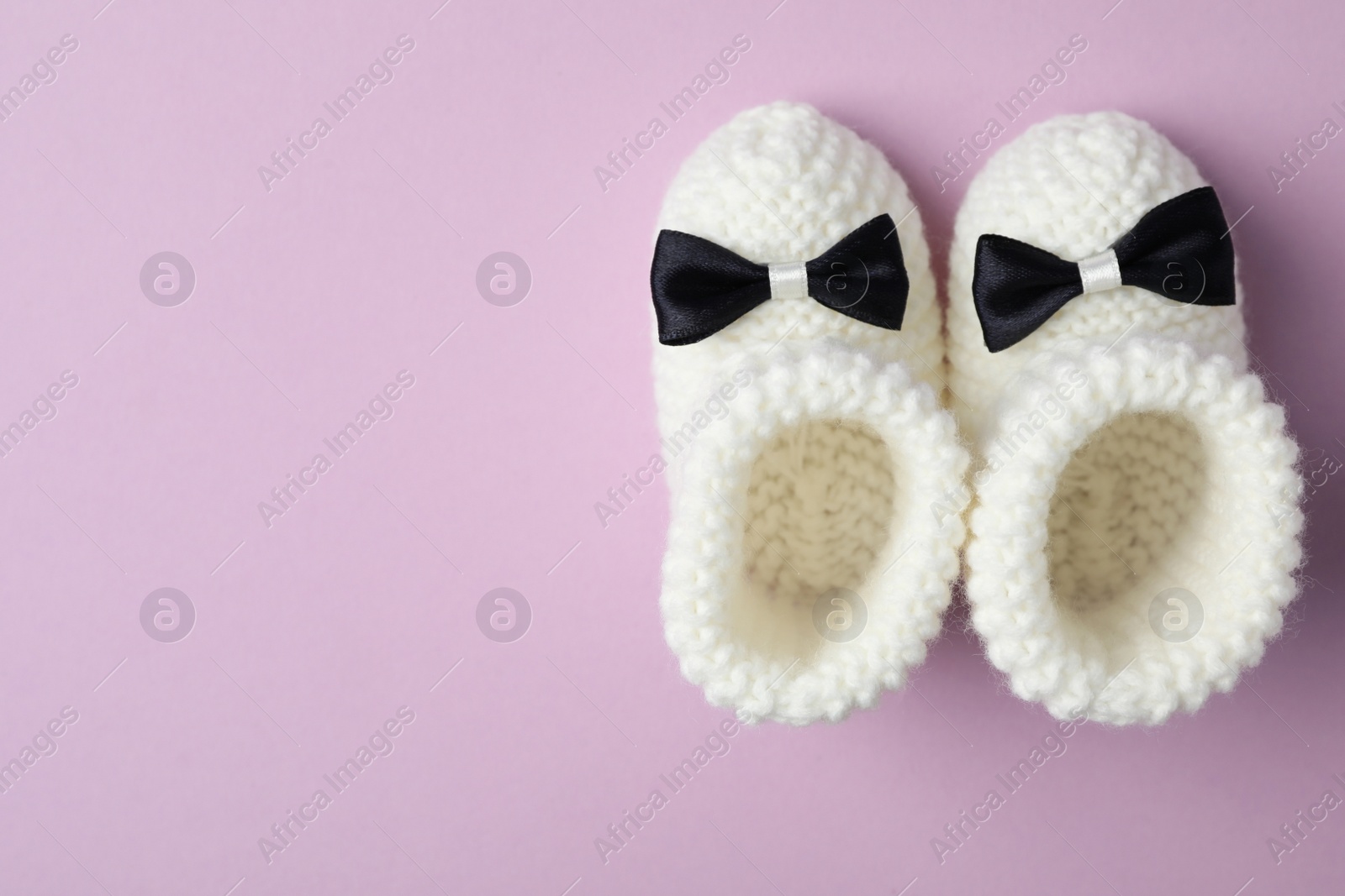 Photo of Handmade child's booties on violet background, flat lay with space for text