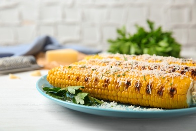 Photo of Plate of grilled corn cobs with grated cheese on white wooden table, closeup