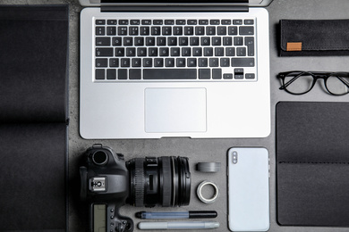 Photo of Flat lay composition with laptop, camera and smartphone on grey stone table. Designer's workplace