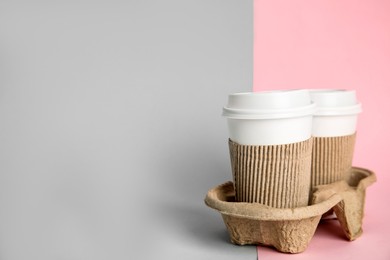 Takeaway paper coffee cups with sleeves and plastic lids in cardboard holder on color background, space for text