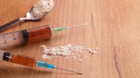 Photo of Powder and syringes on wooden table, closeup with space for text. Hard drugs