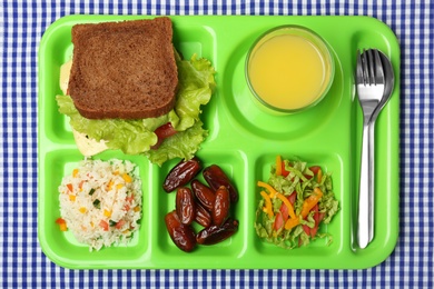 Serving tray with healthy food on tablecloth, top view. School lunch