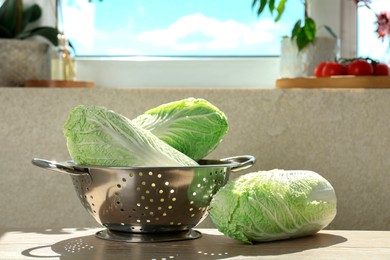 Fresh Chinese cabbages and colander on light wooden table indoors