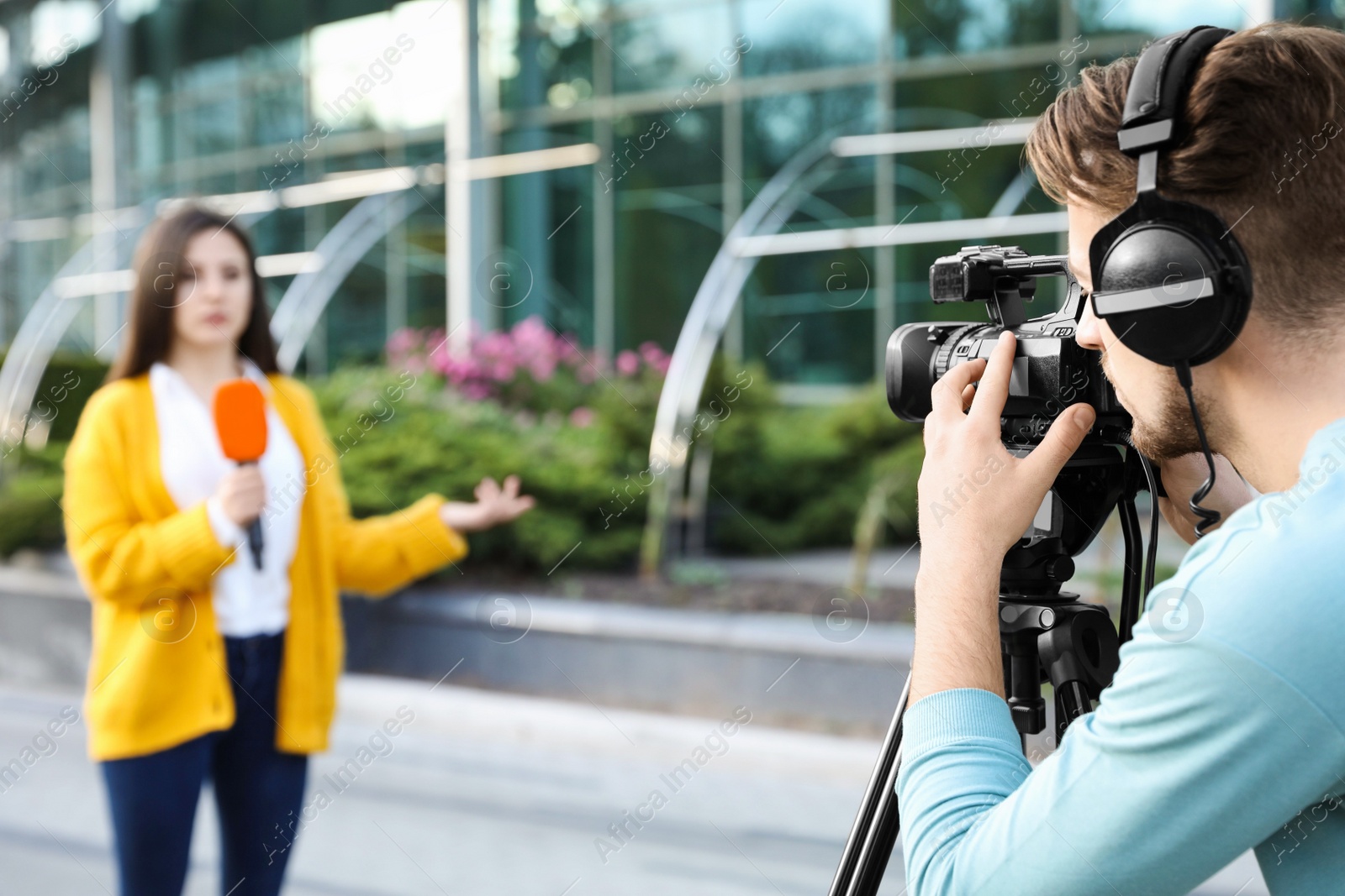 Photo of Young journalist and video operator working on city street. Space for text