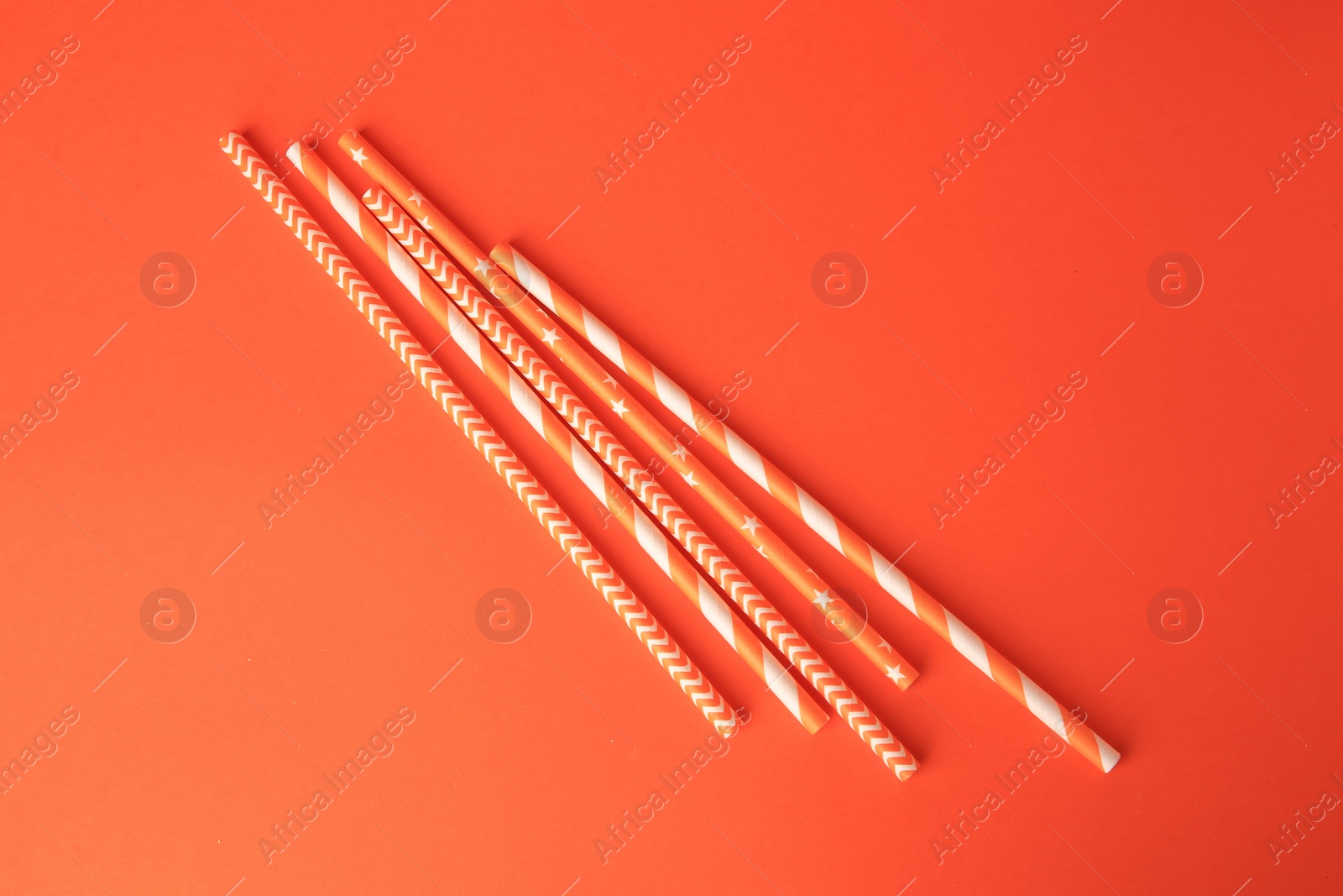 Photo of Striped paper drinking straws on orange background, flat lay