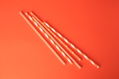 Striped paper drinking straws on orange background, flat lay