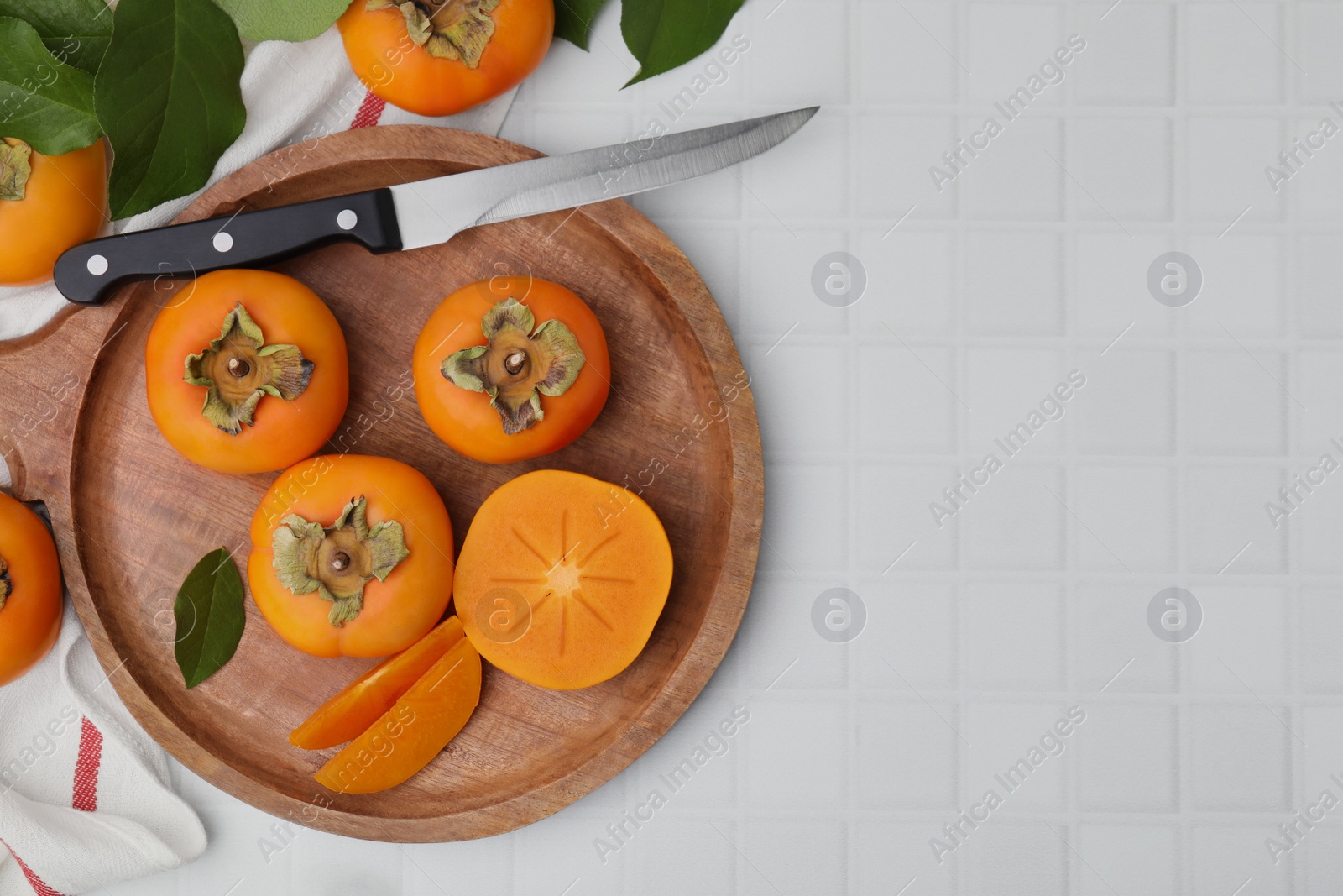 Photo of Delicious ripe persimmons and knife on white table, flat lay. Space for text