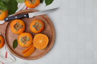 Delicious ripe persimmons and knife on white table, flat lay. Space for text