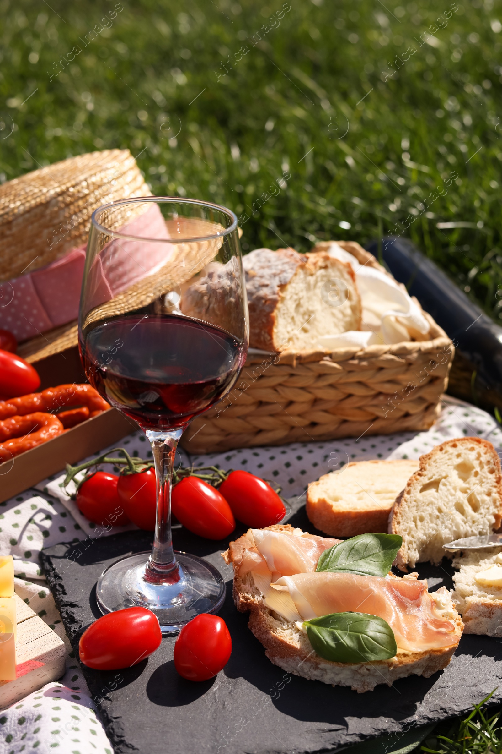 Photo of Blanket with wine and snacks for picnic on green grass