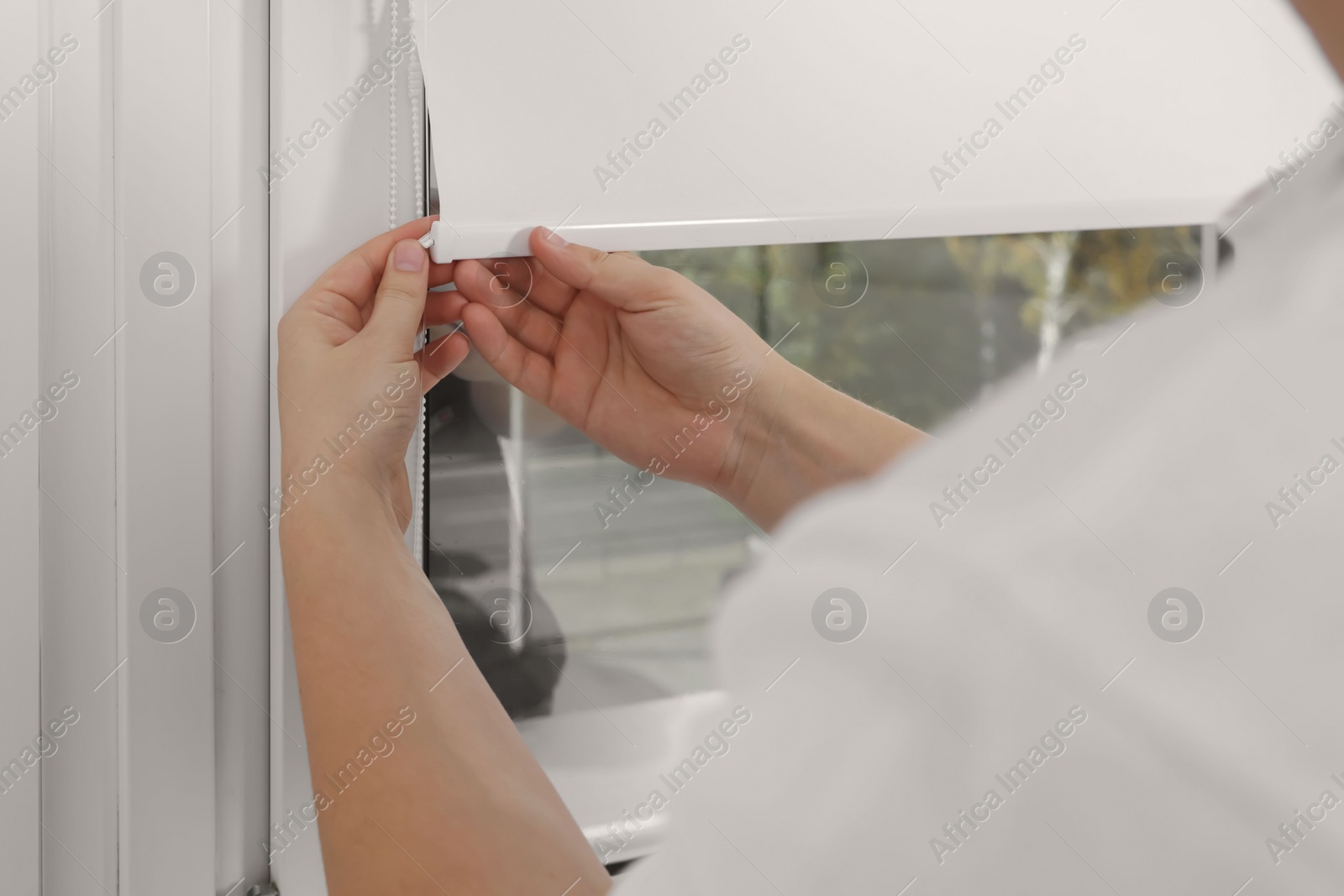 Photo of Worker installing roller window blind indoors, closeup