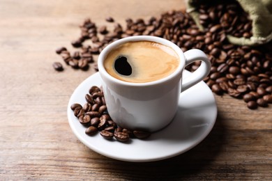 Cup of hot aromatic coffee and roasted beans on wooden table