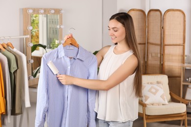 Photo of Young woman cleaning clothes with adhesive lint roller indoors