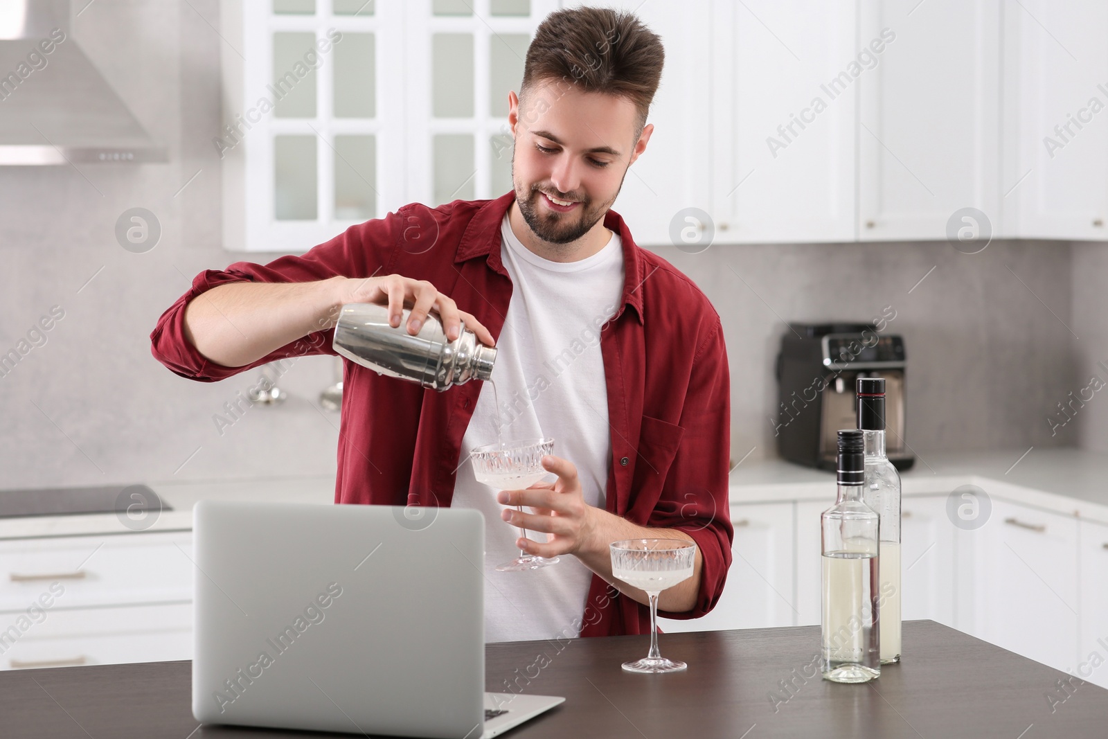 Photo of Man learning to make cocktail with online video on laptop at table in kitchen. Time for hobby