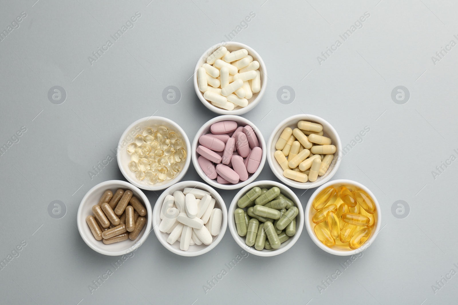 Photo of Different vitamin pills in bowls on grey background, flat lay