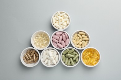 Photo of Different vitamin pills in bowls on grey background, flat lay