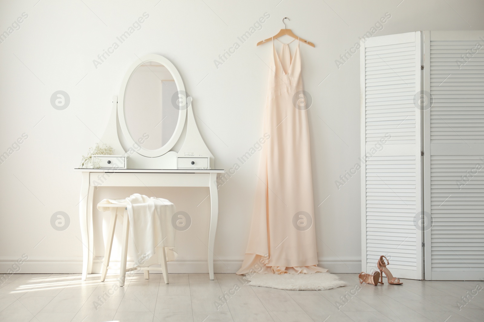 Photo of Beautiful wedding gown hanging near dressing table in room