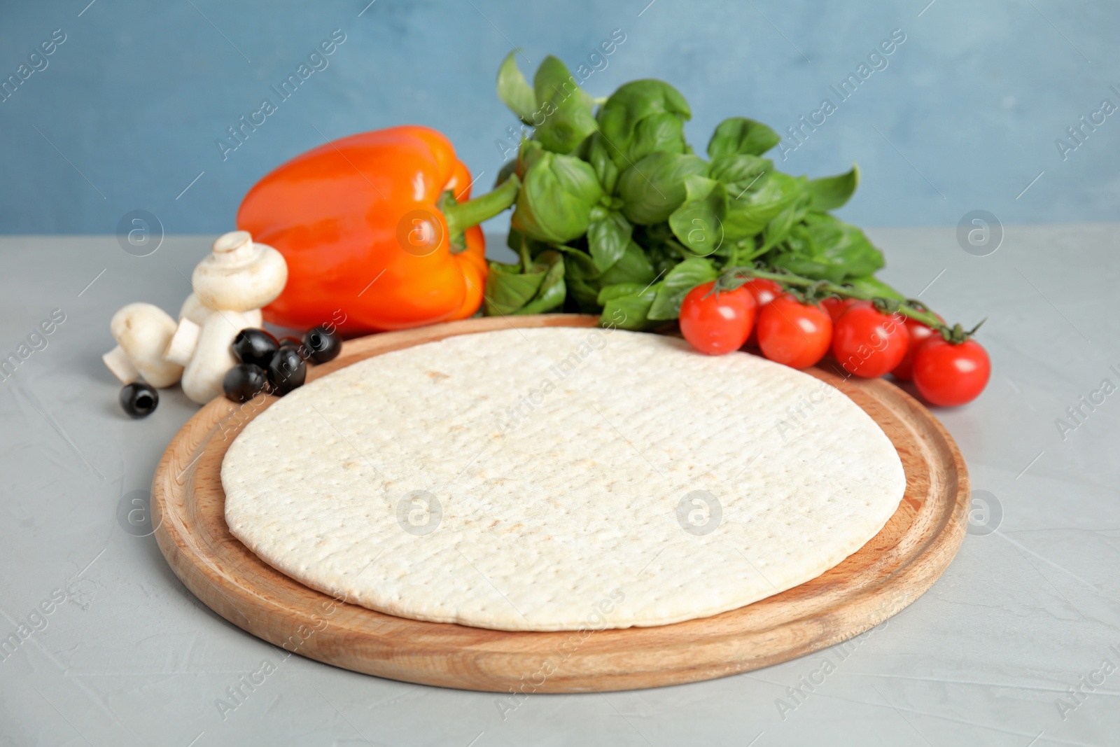 Photo of Base and ingredients for pizza on table against color background