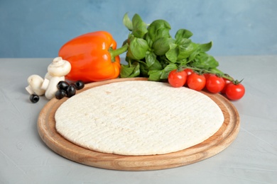 Photo of Base and ingredients for pizza on table against color background