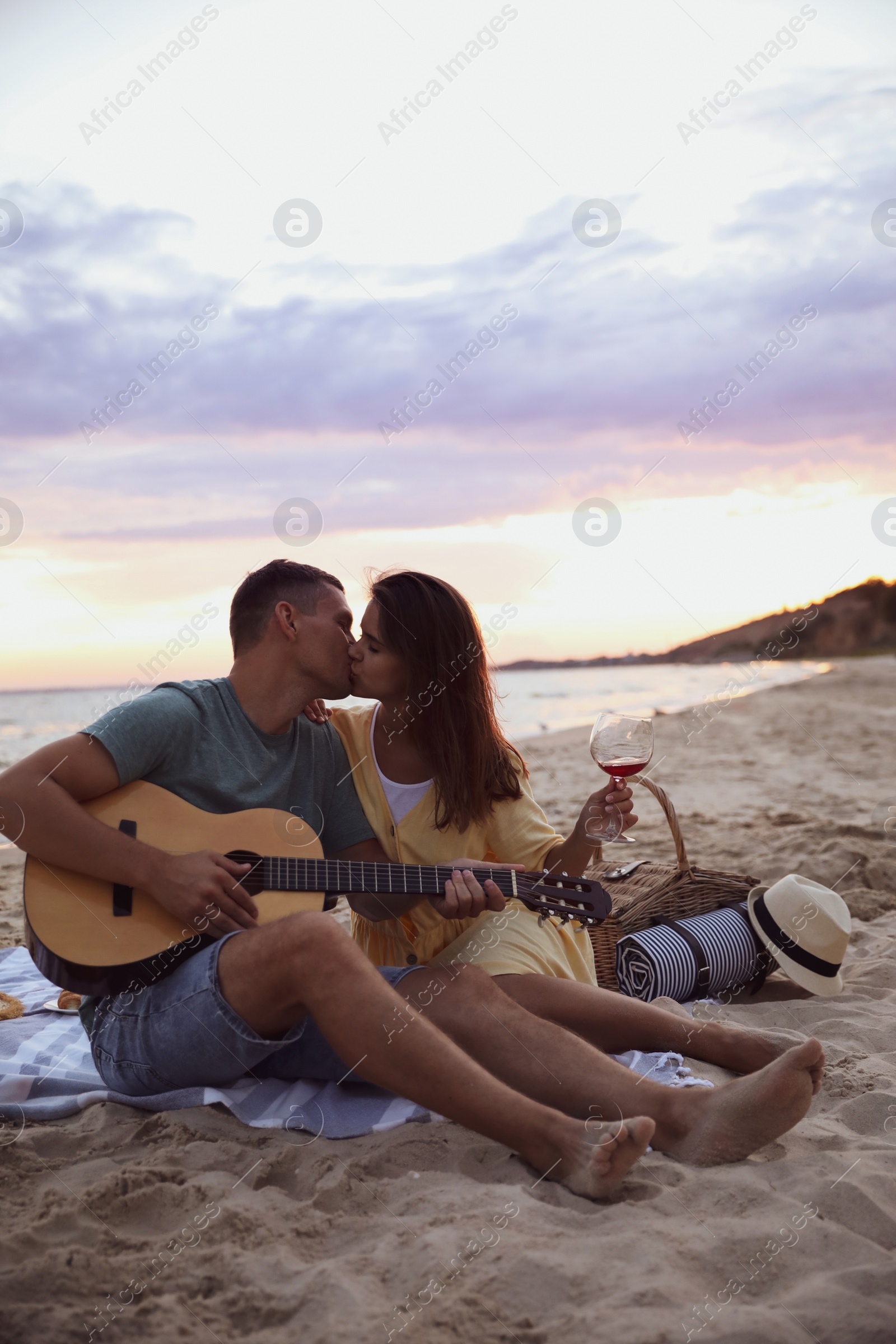 Photo of Lovely couple with guitar and picnic basket on beach at sunset